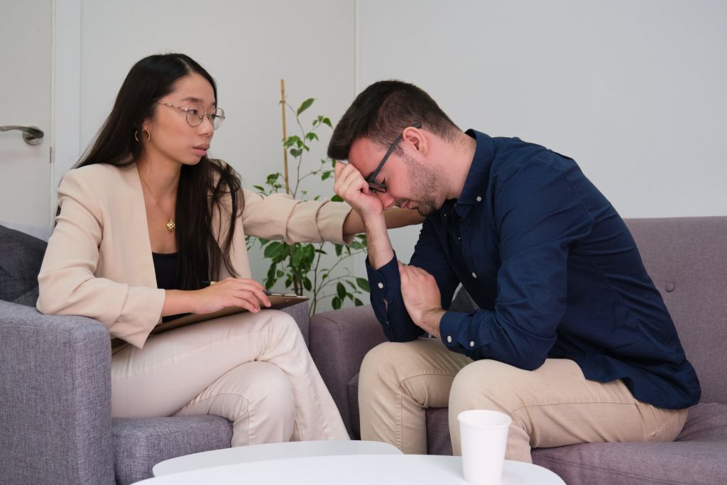 Asian female psychologist comforting her caucasian man patient at therapy.